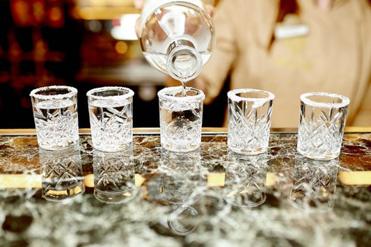 bartender pouring blanco tequila in five shot glasses on bar