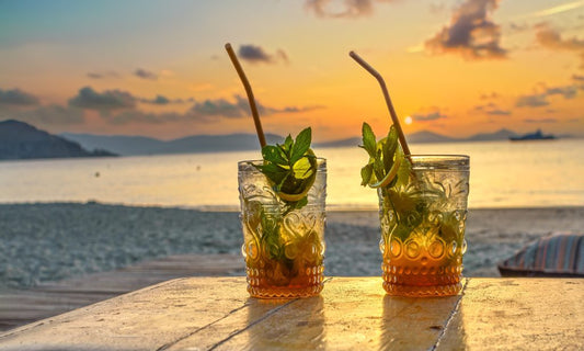 two glasses of mojitos with rum on table by ocean at sunset