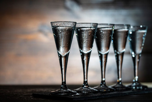 five shot glasses with handles of vodka on wooden bar