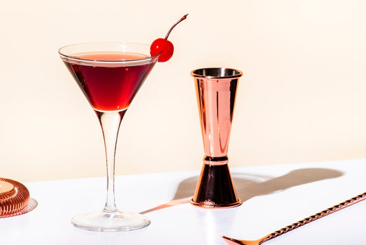 black manhattan cocktail in martini glass with bar tools and cherry