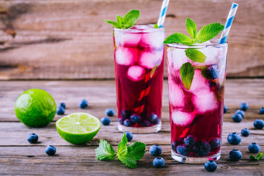 two blueberry vodka cocktails with blueberries and limes on wooden table with wooden background