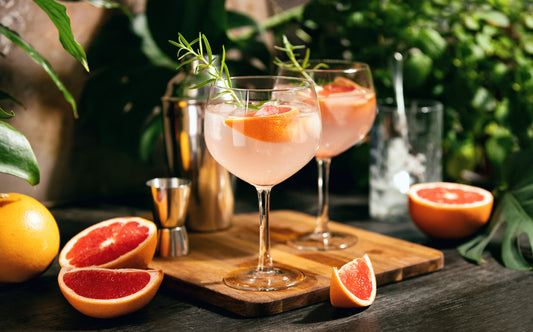 gin cocktail in two glasses on wooden cutting board with sliced grapefuits