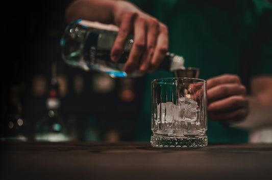 bartender pouring whiskey in glass with ice on bar