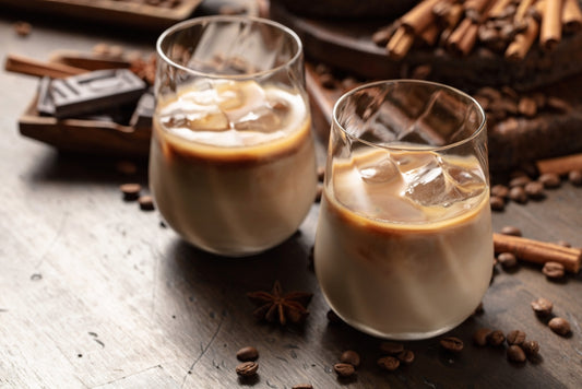two glasses of iced irish cream with chocolate and cinnamon sticks on wooden table