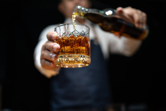man pouring whiskey into glass with black background