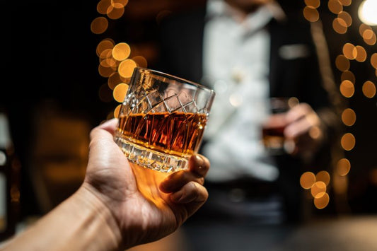 a tilted glass of laws whiskey in front of a man in a suit