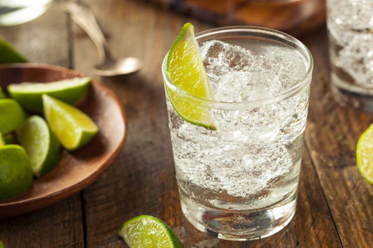 gin and tonic with ice and lime on wooden table with sliced limes