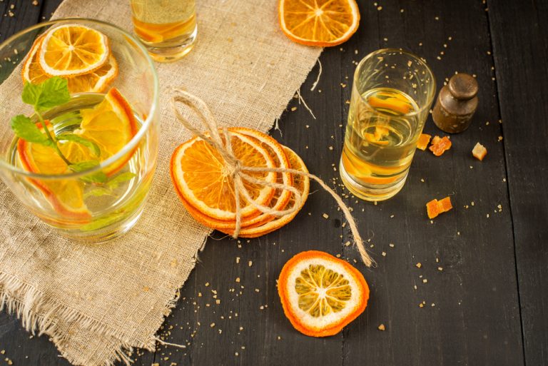 orange liqueur in glass with sliced oranges on dark wooden table