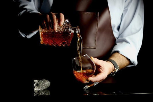 man in apron pouring cognac from bottle into glass