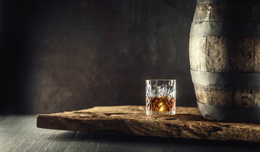 whiskey in glass on wooden board by barrel