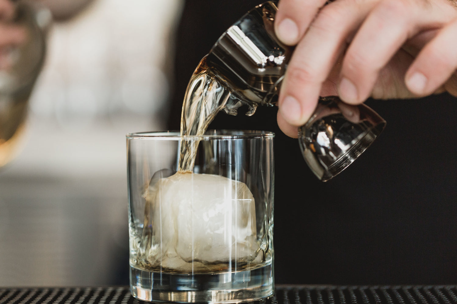 hand pouring alcohol with jiggle into glass with ice