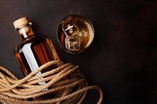 bottle of rum next to glass of whiskey on dark table