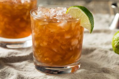 dark rum cocktails with ice and lime wedges on sand