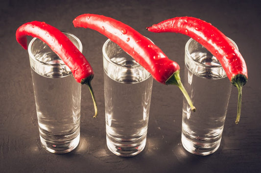 three shot glasses of au vodka with red peppers on bar