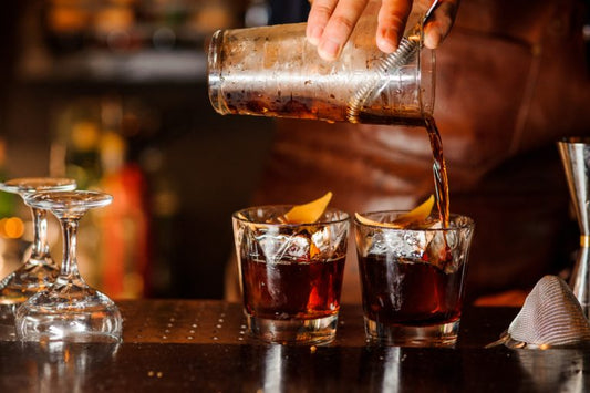 bartender making a summer bourbon cocktail in two glasses in bar