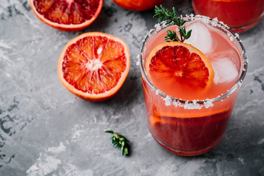 blood orange cocktail in glass with sliced blood oranges on marble table