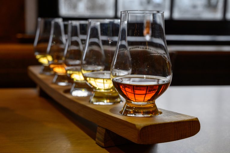 flight of different colored flavored whiskey shots on bar