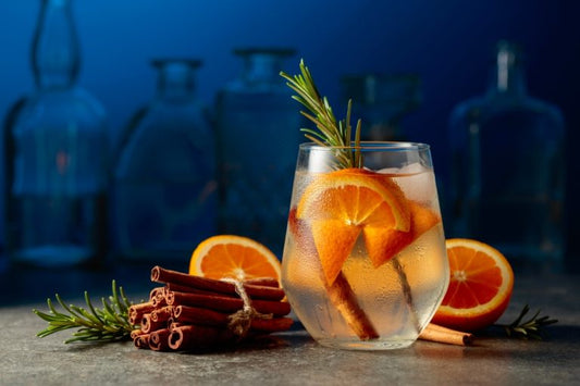 sloe gin cocktail in glass with orange slices and cinnamon sticks in front of empty bottles