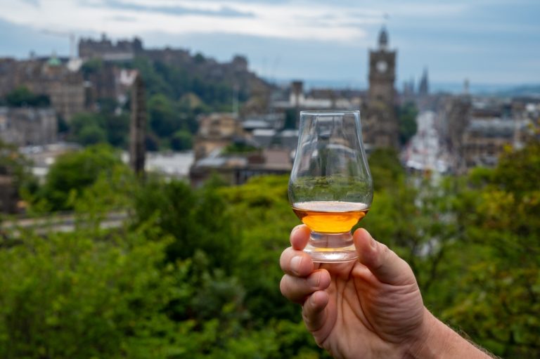 glass of single malt scotch being held in front of scottish landscape