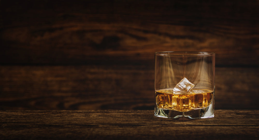 glass of bourbon and ice on wood with wooden background