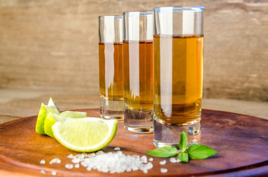 three glasses filled with extra anejo tequila by sliced limes and salt