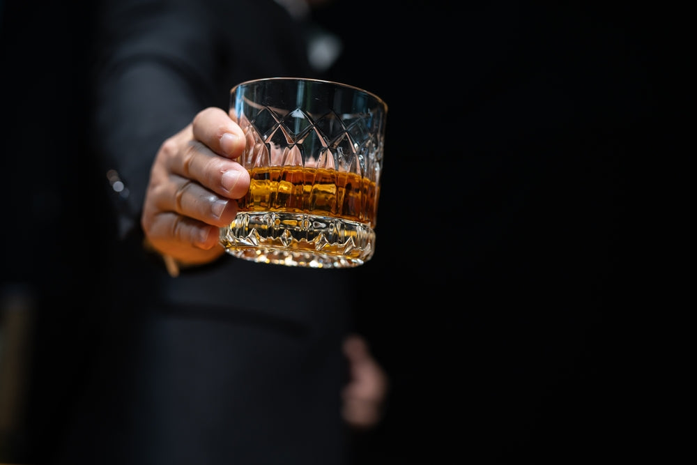 hand holding whiskey glass with dark background