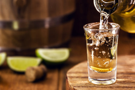 mezcal being poured into shot glass with limes on bar