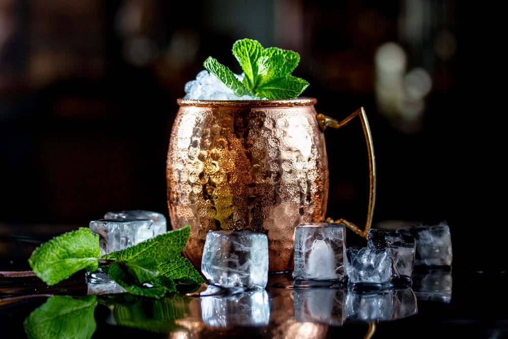 moscow mule in copper mug with ice cubes on black bar