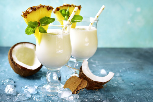 two rumchata cocktails with pineapples and coconuts on blue table with blue background