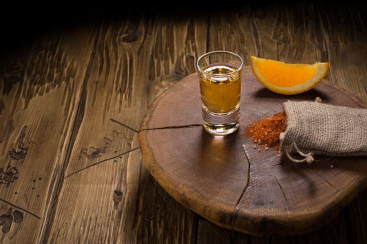 shot glass of mezcal with orange slices, chili pepper and worm salt on a old wooden table