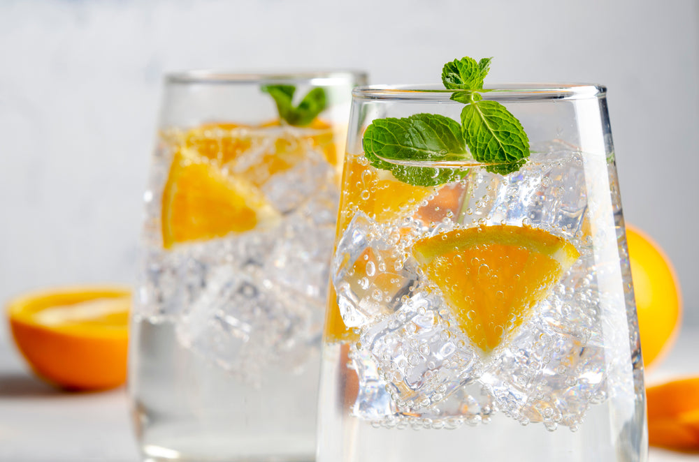 glass of play hard seltzer with sliced limes on gray table