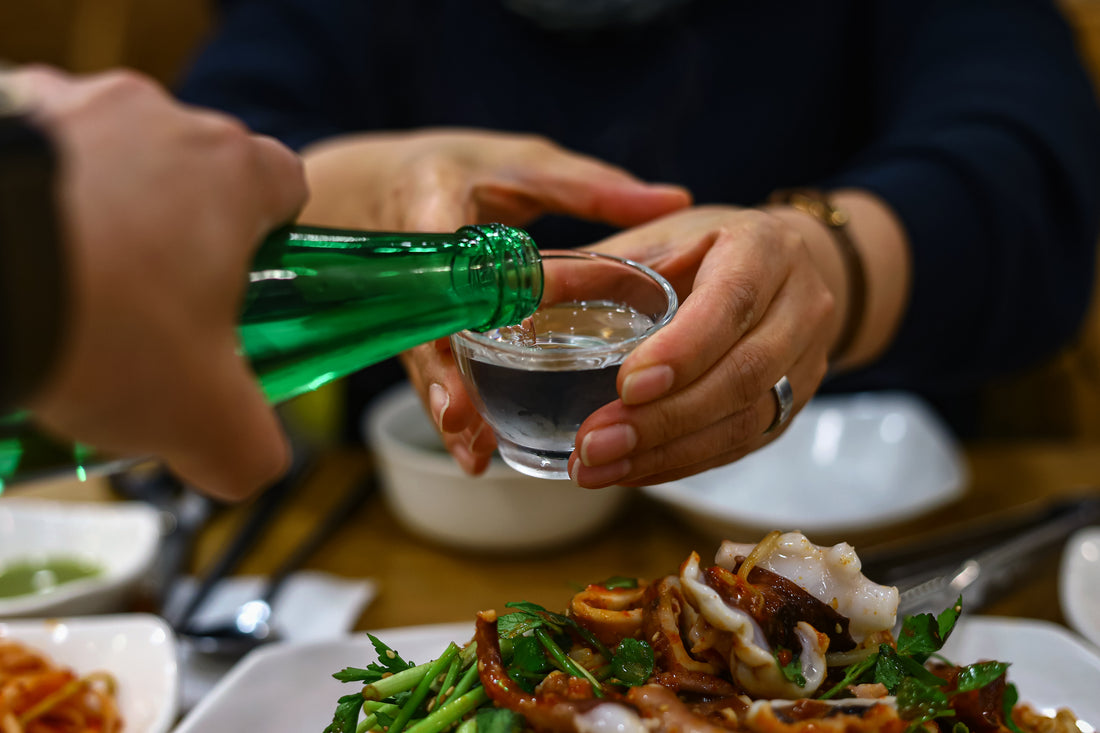 hand pouring a soju cocktail into a glass held by person above a dinner table