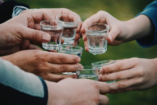 group of people clinking shot glasses of vodka in circle