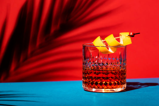 sazerac in a bourgon glass with fruit garnish in front of palm leaf