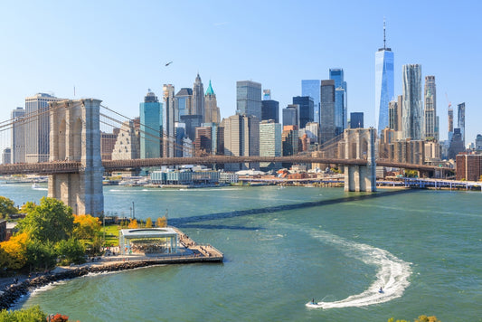 nyc skyline with bridge and a river with a boat leaving a wake behind