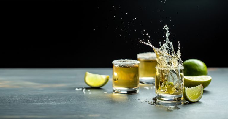 three tequila shots, one splashing, with lime and salt