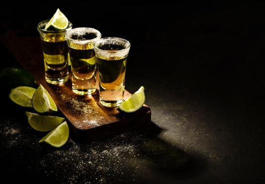 three tequila shots with limes on wooden serving board