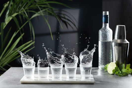 flight of vodka shot glasses with vodka splashing out near bar tools