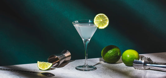 vodka gimlet with lemon in cocktail glass on white table with garnishes