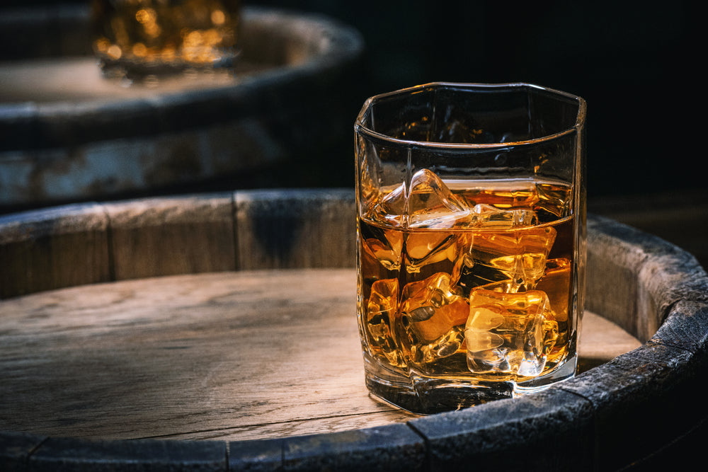 whiskey in glass with ice on wooden barrel in dark